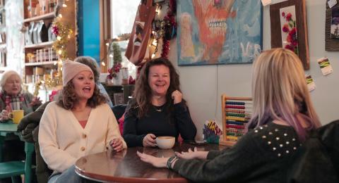 Three women sitting at a table inside of Grackle Coffee enjoying hot drinks and laughing